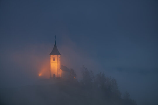 A scenic view of The Church of St. Primoz and Felicijan, Jamnik, Slovenia. The Jamnik Church is a charming 15th-century chapel in the Kamnik-Savinja Alps near Kranj. Autumn foggy early morning.