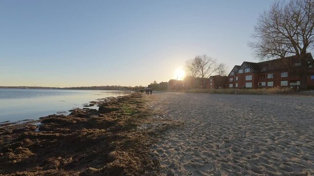 Wide view of Eckernfoerde beach at sunset with calm Baltic Sea shoreline and houses along the coast in warm evening light