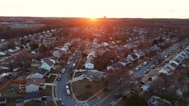 Aerial view of American suburban neighborhood at sunset in winter, warm golden light over single family houses, quiet streets and residential blocks. Wide shot. Beautiful red sky at dusk in USA.