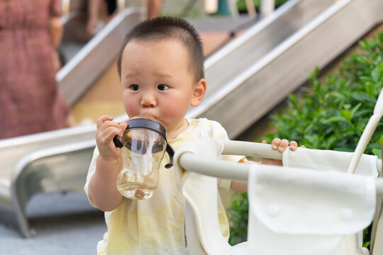Young Asian boy drinking water from a baby bottle outdoors in summer