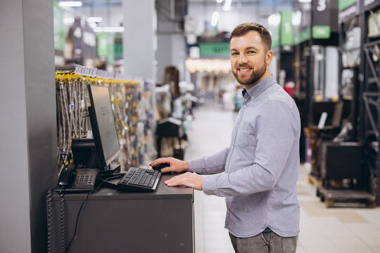 Friendly retail worker smiling, standing at a counter with a computer, providing customer service in a DIY shop