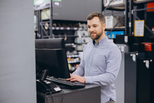 Retail worker managing store inventory using a computer at a service desk, providing customer support