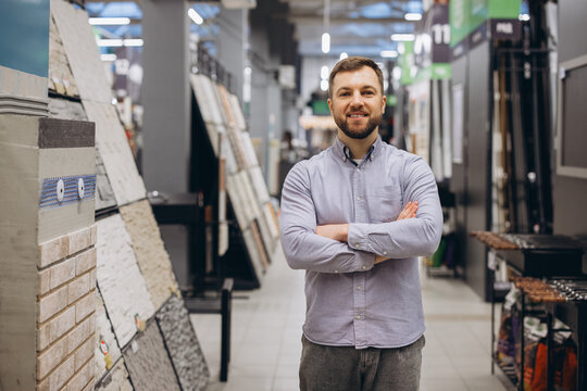 Smiling man standing with crossed arms in a building materials store showroom, selling renovation supplies