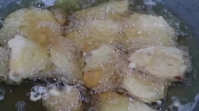 Deep frying sliced sweet potato in hot oil inside a wok. Popular Indonesian snack known as Ubi goreng