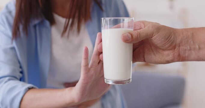 Lactose intolerance of woman suffering from allergic gastrointestinal symptoms, stomach pain and cramps, nausea. Girl holding belly, refusing milk glass with stop gesture, lactose free diet at home