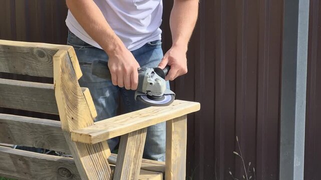 A man sends a homemade wooden bench using a grinder tool.