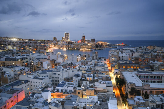 Aerial view of the city lights reflecting on the water around Sliema, illuminating the Maltese skyline with a soft, ethereal glow, Sliema, Sliema, Malta.
