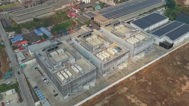High angle drone footage showing a contemporary data center complex. The buildings feature modern architecture with visible cooling systems and solar panels