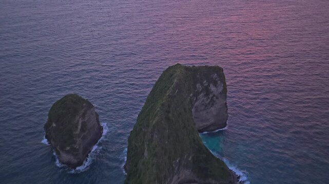 Amazing aerial shot flying away from the stunning kelingking beach, shaped like a t rex, revealing a beautiful and colorful sunset sky