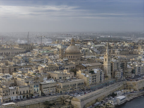 Aerial view of golden-stone buildings huddle beneath a vast dome, framed by the ancient city walls and the endless sea, Valletta, Valletta, Malta.