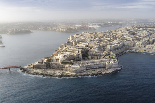 Aerial view of the ancient Fort St Elmo walls meet the deep blue sea, a historic city unfolds with warm stone buildings and distant ships, Valletta, Valletta, Malta.