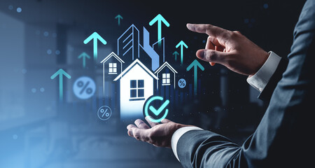 Businessman hand holding digital house model with rising arrows and building icons on futuristic...