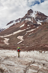 Naklejka premium Climbing Mount Kazbek. Hiker walks on glacier near mountain with snow under cloudy sky in the Andes during late afternoon