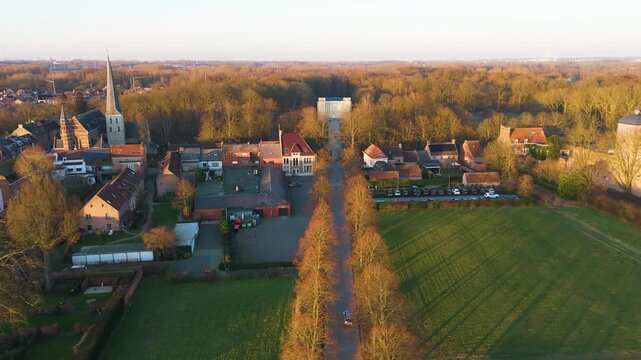 golden hour panorama bornem tree lined avenue through green fields d&rsquo;ursel castle distance village church spire clustered houses glowing forest reveals toward wide drone belgium 