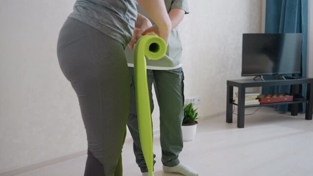 Teamwork as lady and son fold bright green yoga mat in modern living room, casual fitness preparation, family cooperation, wellness activity, showing unity