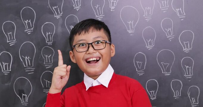 Schoolboy Getting a Bright Idea in Front of Blackboard with Light Bulb Sketches