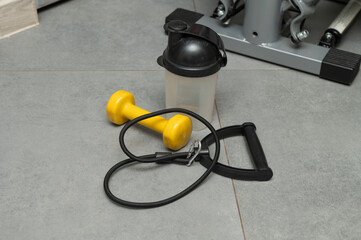 Home workout essentials: dumbbell, resistance tube, and shaker on grey tile floor