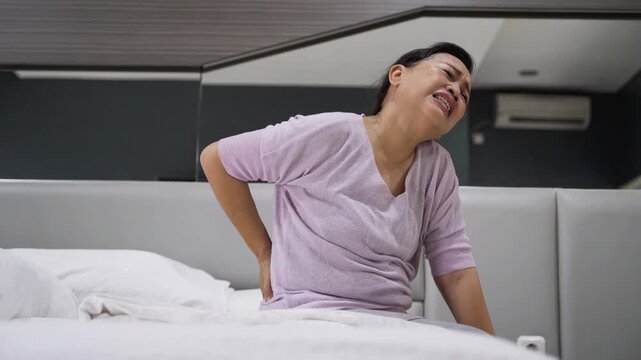 Senior Asian Woman Suffering from Acute Lower Back Pain While Sitting on Bed