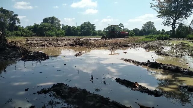 Tractor Plowing Muddy Paddy Field in Rural Sri Lanka, Traditional Rice Farming Agriculture
