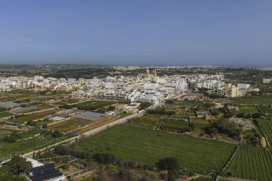 Aerial view of the town with its church steeple rising, surrounded by a patchwork of verdant fields under a vast sky, Dingli, Dingli, Malta.