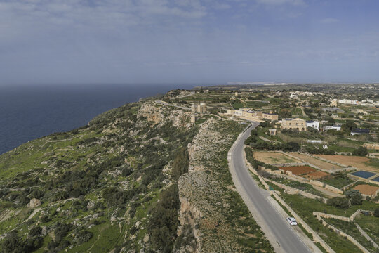 Aerial view of rugged cliffs meet the azure sea, with a winding road cutting through the landscape, Dingli, Malta.