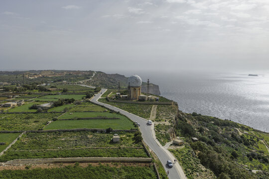 Aerial view of the serene landscape where a road winds towards the iconic Dingli Radar Station perched dramatically on the cliff's edge, Dingli, Malta.