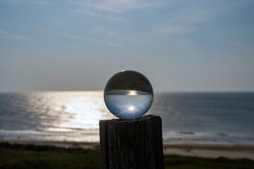 Ball made of glass lies on a wooden post in which the beach and the sea are reflected