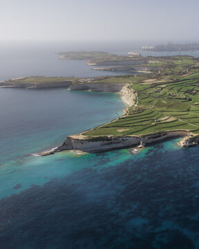 Aerial view of rugged Munxar Path meet the turquoise waters of the Mediterranean Sea, juxtaposed against the verdant green fields, Marsaskala, Marsaskala, Malta.