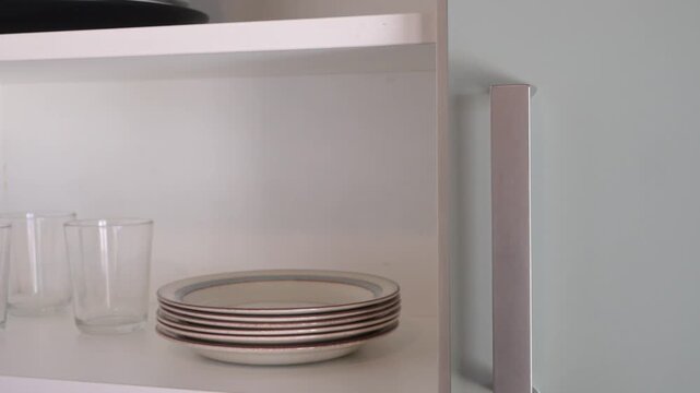Hand opening a kitchen cabinet and taking a plate from a stack. Home kitchen routine and household organization concept, clean domestic lifestyle b-roll.
