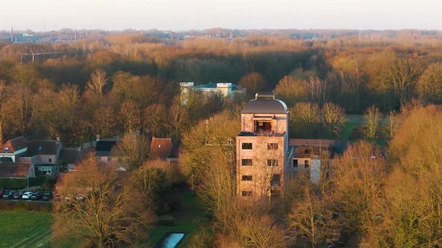 golden hour bornem tall brick observation tower glowing warm sunlight above treetops village rooftops forest stretching into horizon up close drone belgium architecture 