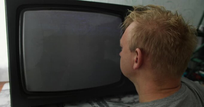 Man fixates on CRT television as it slowly powers with analog TV static. Obsessive viewing behavior, distorted perception, and psychological tension linked to media exposure