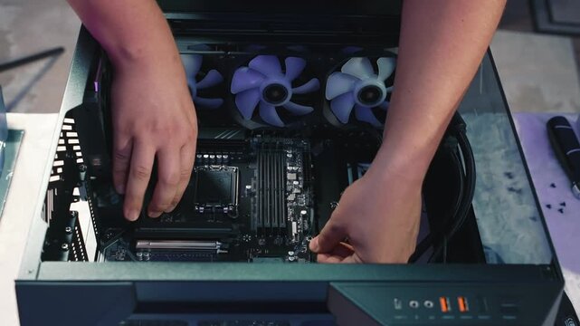Installing the motherboard into a desktop PC case, top-down view. Visible fans, cables, and ports prepared for connection. Part of the system build process
