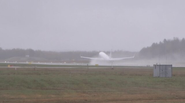 airplane aircraft rotates departs rain soaked runway oslo airport disappearing into heavy mist plume water spray trails behind from broad norway gardermoen takeoff rotation 
