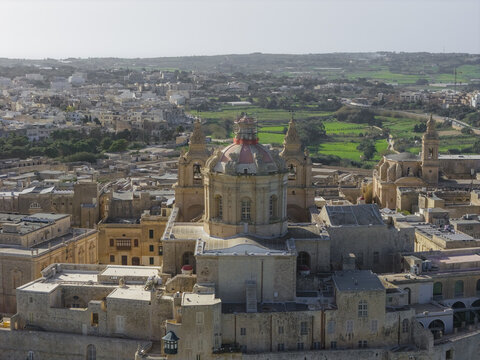 Aerial view of the imposing Mdina Cathedral with its striking dome dominating the skyline amidst a sea of sandstone buildings, Rabat, Mdina, Malta.