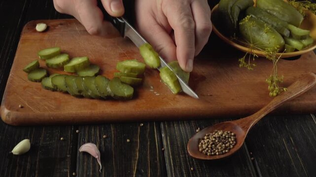 Slicing pickles on a wooden cutting board with garlic and spices visible, showcasing the progression of food preparation in a kitchen setting