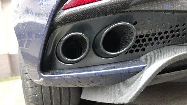 rear lower bumper twin circular exhaust tips set within dark diffuser hexagonal mesh insert carbon fiber trim road worn textures visible beneath blue sports up close tailpipes 
