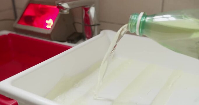 Preparing chemical trays in darkroom by pouring photographic chemicals for analog photo printing workflow
