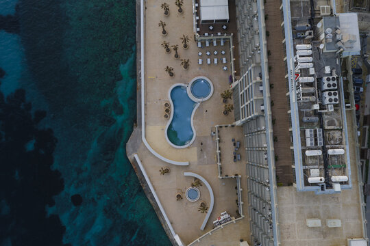 Aerial view of a luxury hotel with turquoise pools contrasting against the beige stone, nestled beside the deep blue sea, St. Julian's, Sliema, Malta.