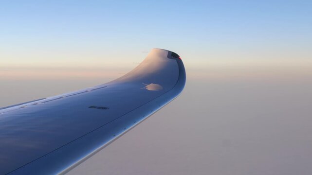 aircraft wing curves above pale cloud layer sunset soft pastel light reflecting off winglet against calm clear sky clouds reflection dusk evening horizon serene flight aviation 