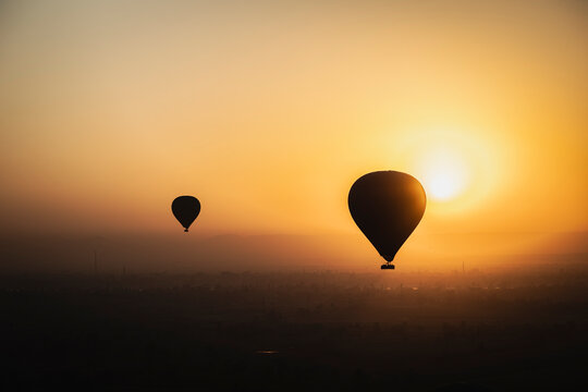  dos globos o balones aerost&aacute;ticos volando por el cielo de Luxor en Egipto con el cielo &aacute;mbar del amanecer