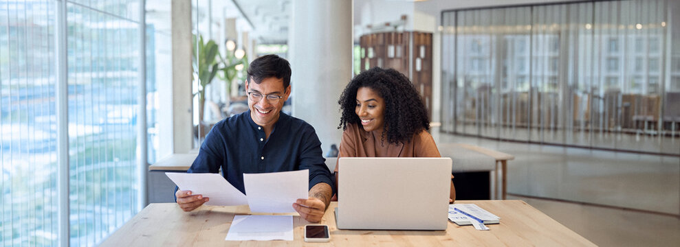 Professional business team of two diverse advisors, employees man and woman, manager and client talking using laptop computer discussing documents working in office at work meeting.