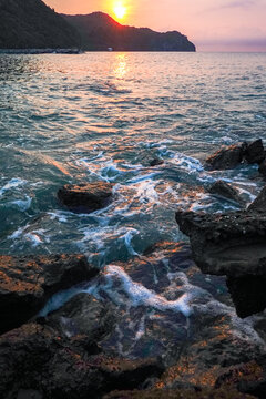 Ocean waves crashing on rocky shores at sunset, golden sunlight reflecting on sea surface, natural seascapes concept of freedom, peace, relaxation, travel, adventure, and nature beauty.