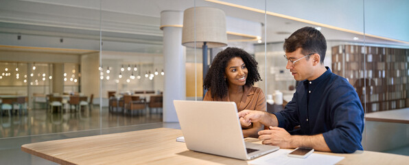 Two young busy diverse coworkers business people using laptop at office meeting. Smiling team...