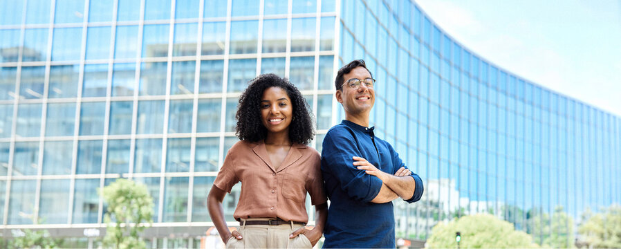 Young happy smiling professional office team of two diverse confident female and male partners business people man and woman standing outdoors on city street looking at camera, corporate portrait.
