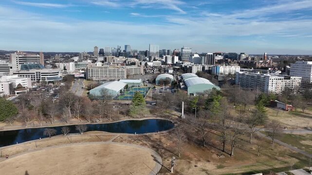 Rising aerial flyover of tNashville Parthenon in winter with downtown skyline in background under clear blue sky at Centennial Park, Tennessee. Tennis courts and calm pond in park. Sunny day. Rising.