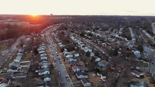 Aerial view of quiet American suburban neighborhood at sunset in winter, with rows of small houses, bare trees and soft golden light stretching across residential streets. Wide shot. Maryland, USA