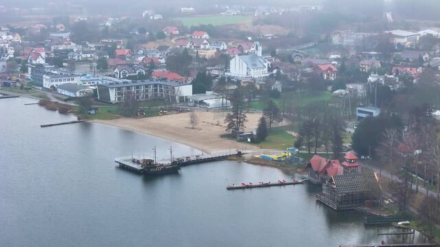soft fog draped panorama charzykowy poland quiet lakeshore wooden pier moored boat empty beach pastel roofed village fading into drone hills mist mini pro aerial roofs scenery landscape 