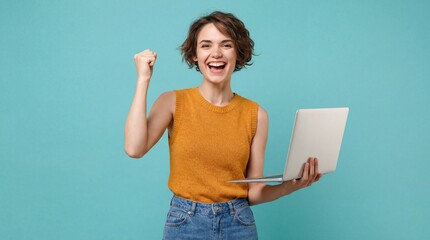 Happy young woman celebrating success while holding laptop against blue studio background