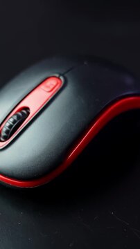Moody macro shot of a black and red computer mouse on a dark desk with copy space, showing the scroll wheel and buttons in warm studio light. Vertical.