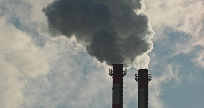 Two industrial stacks of a gas boiler plant emitting water vapor. White steam plume and condensation drift across a deep blue sky, concept of urban heating infrastructure.